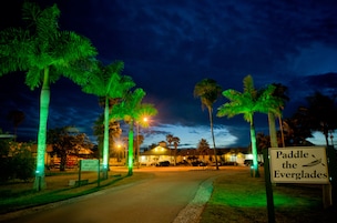 A sign for 'Paddle the Everglades' with palm trees and street lights.