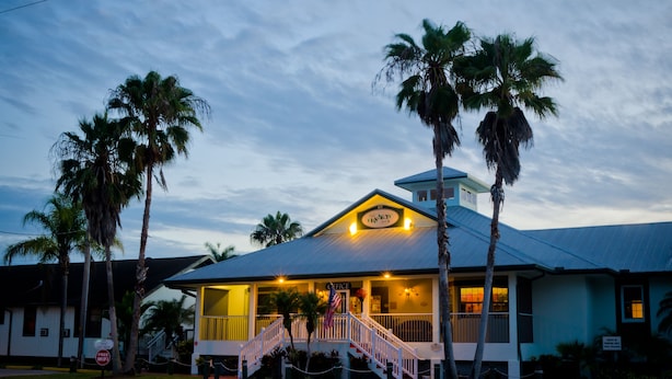 A building with a porch, stairs, and palm trees.