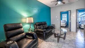A living room with teal walls, a ceiling fan, a leather sofa, a glass coffee table, and a lamp.