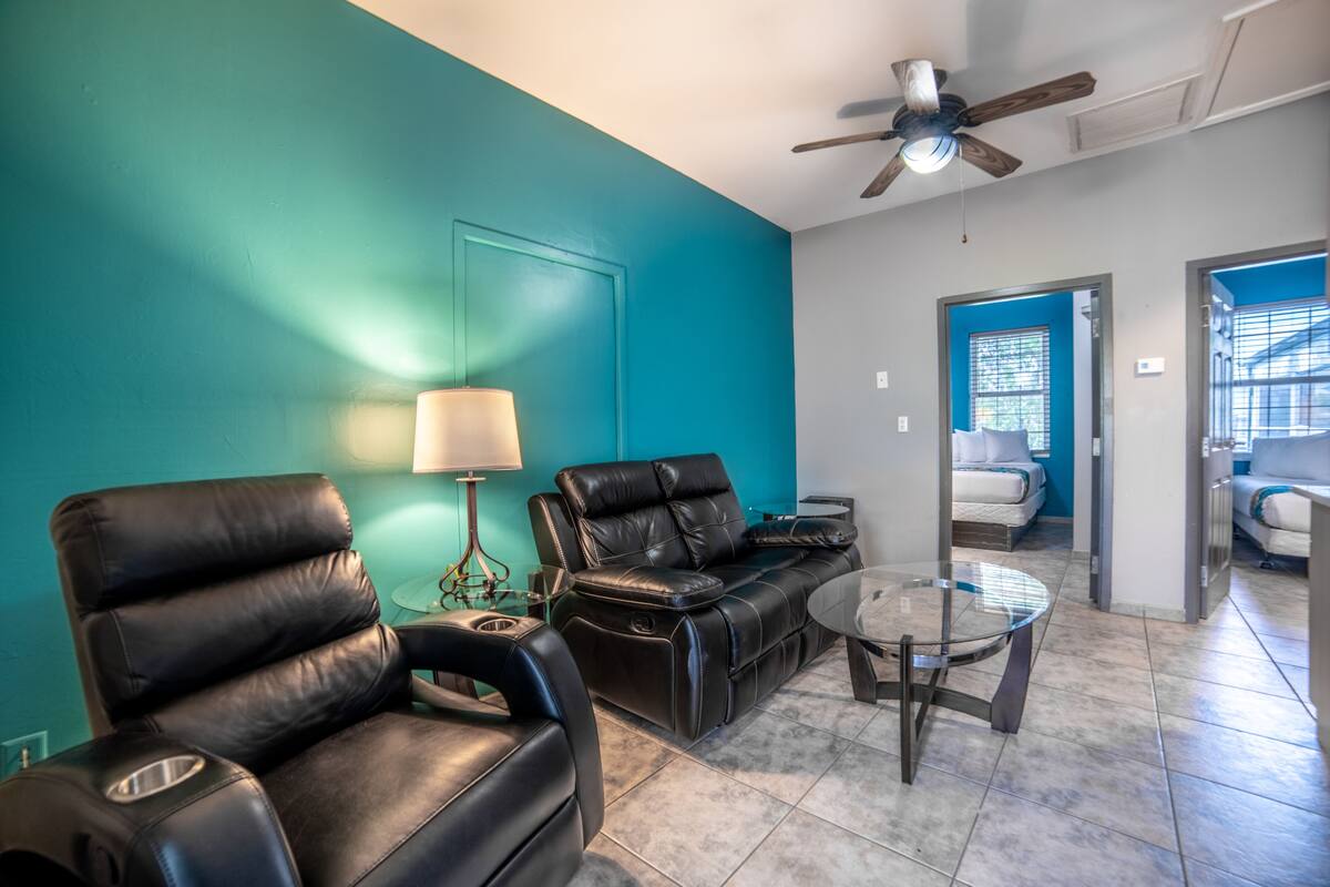 A living room with teal walls, a ceiling fan, a leather sofa, a glass coffee table, and a lamp.