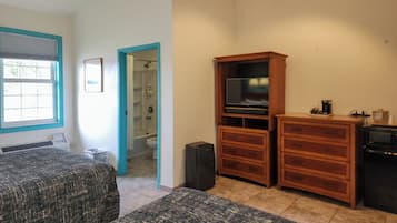 Een kamer met twee bedden, een houten kastje met een televisie, en een badkamer zichtbaar door een open deur.