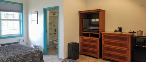 Una habitación con dos camas, un mueble de madera con un televisor, y un baño visible a través de una puerta abierta.