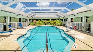 An indoor swimming pool with a glass ceiling, surrounded by lounge chairs and a white fence.