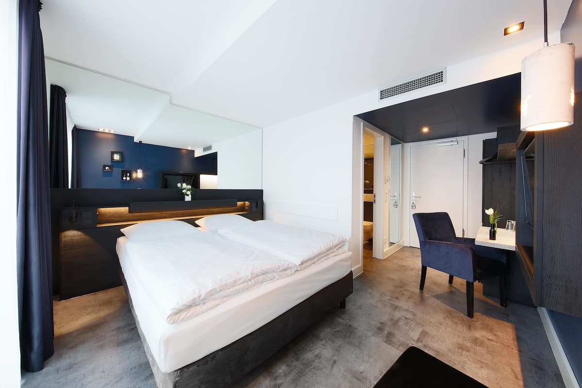 Une chambre d’hôtel moderne avec un grand lit, un bureau, une chaise et un miroir.
