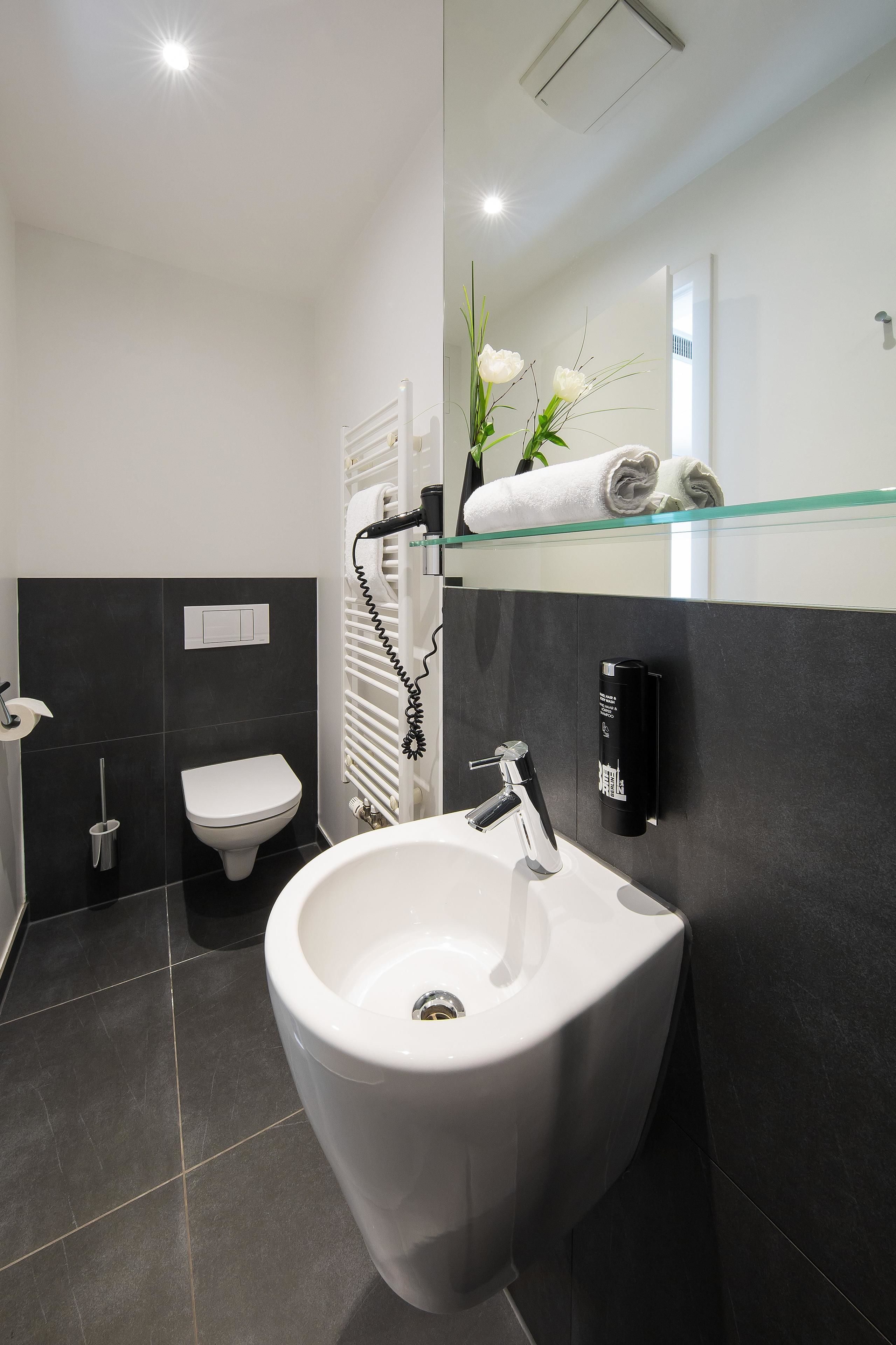 Un baño moderno con un bidé, un inodoro y un estante de vidrio con toallas.