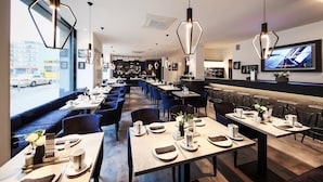Un restaurante moderno con lámparas colgantes hexagonales, mesas ordenadas con vajilla blanca y un televisor grande en la pared.