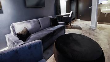 A modern living room with a dark blue sofa, a round ottoman, and a flat-screen TV mounted on the wall.