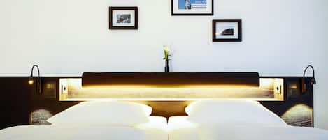 Un lit bien fait, avec du linge de lit blanc, une table de chevet avec une lampe et des tableaux encadrés au mur.