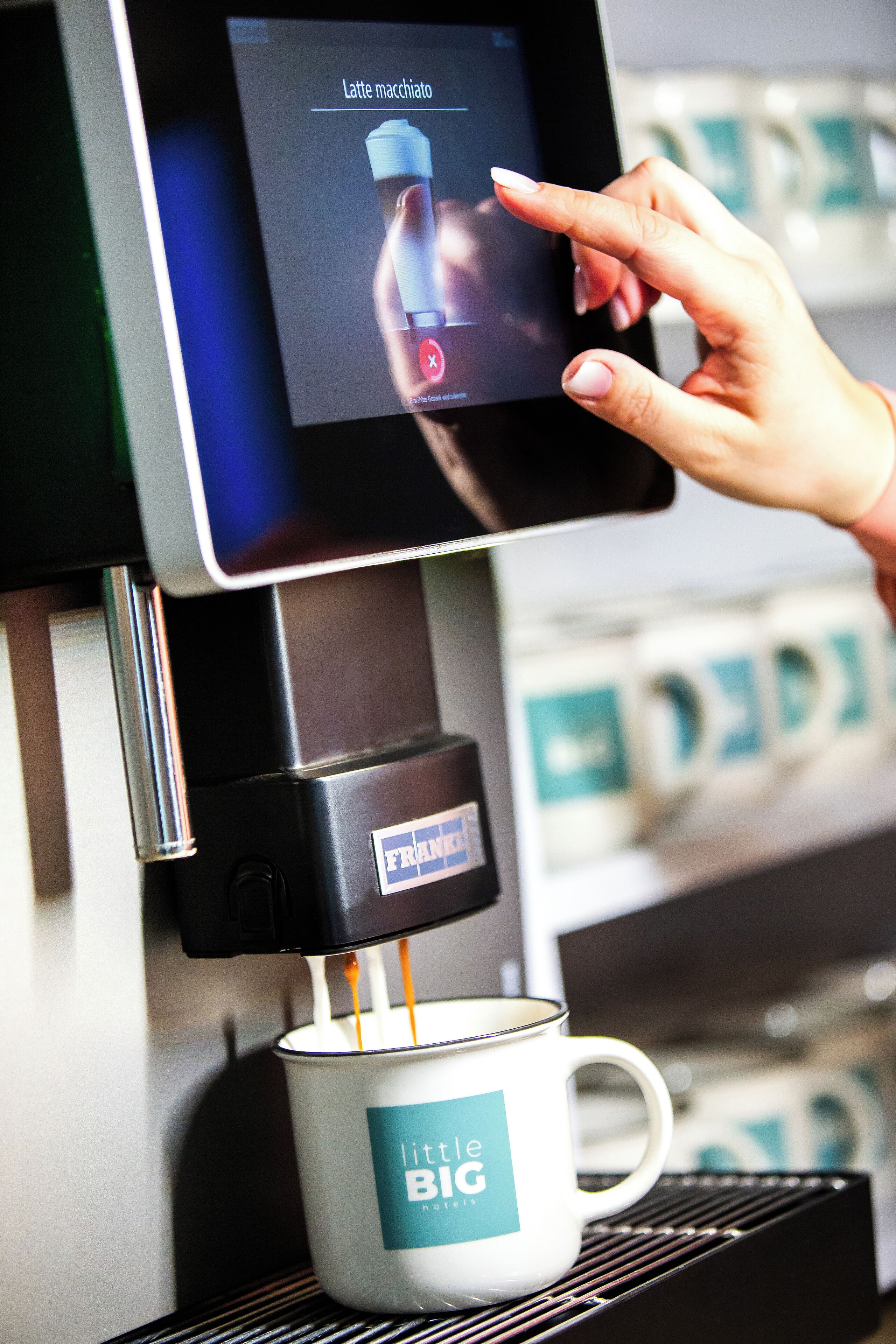 A coffee machine dispensing a latte macchiato into a branded mug.