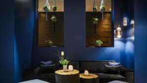 Un área de estar moderna con paredes azul oscuro, un sofá de cuero negro y mesas redondas de madera con plantas en macetas.