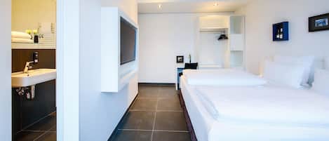 Une chambre d’hôtel moderne dotée d’un grand lit, d’un téléviseur fixé au mur, d’une armoire intégrée et d’une salle de bain avec un lavabo et un miroir.