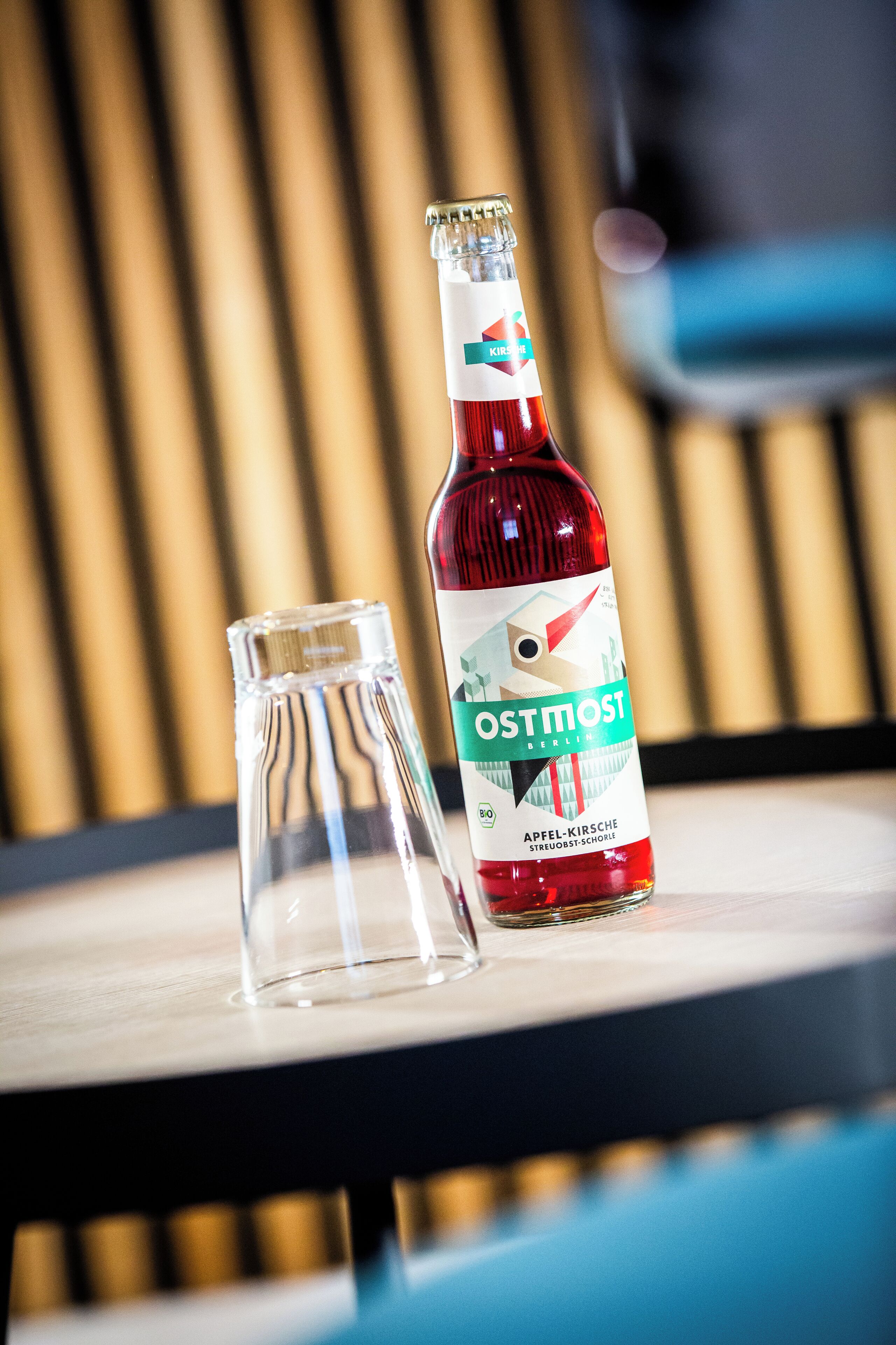 Een fles Ostmost bier en een helder glas op een tafel, met een wazige achtergrond.