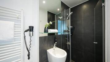 Un baño moderno con un bidé, una cabina de ducha de vidrio y un perchero para toallas.