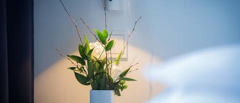 Un florero blanco con hojas verdes y flores blancas sobre una mesa.