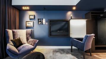 Una sala de estar moderna con un televisor de pantalla plana grande montado en la pared, dos sillones cómodos, una mesita auxiliar con un florero y una pared de acento azul oscuro.