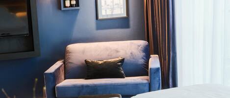 Una habitación de hotel moderna con una pared azul, un sofá gris, una mesita y un jarrón con flores blancas.