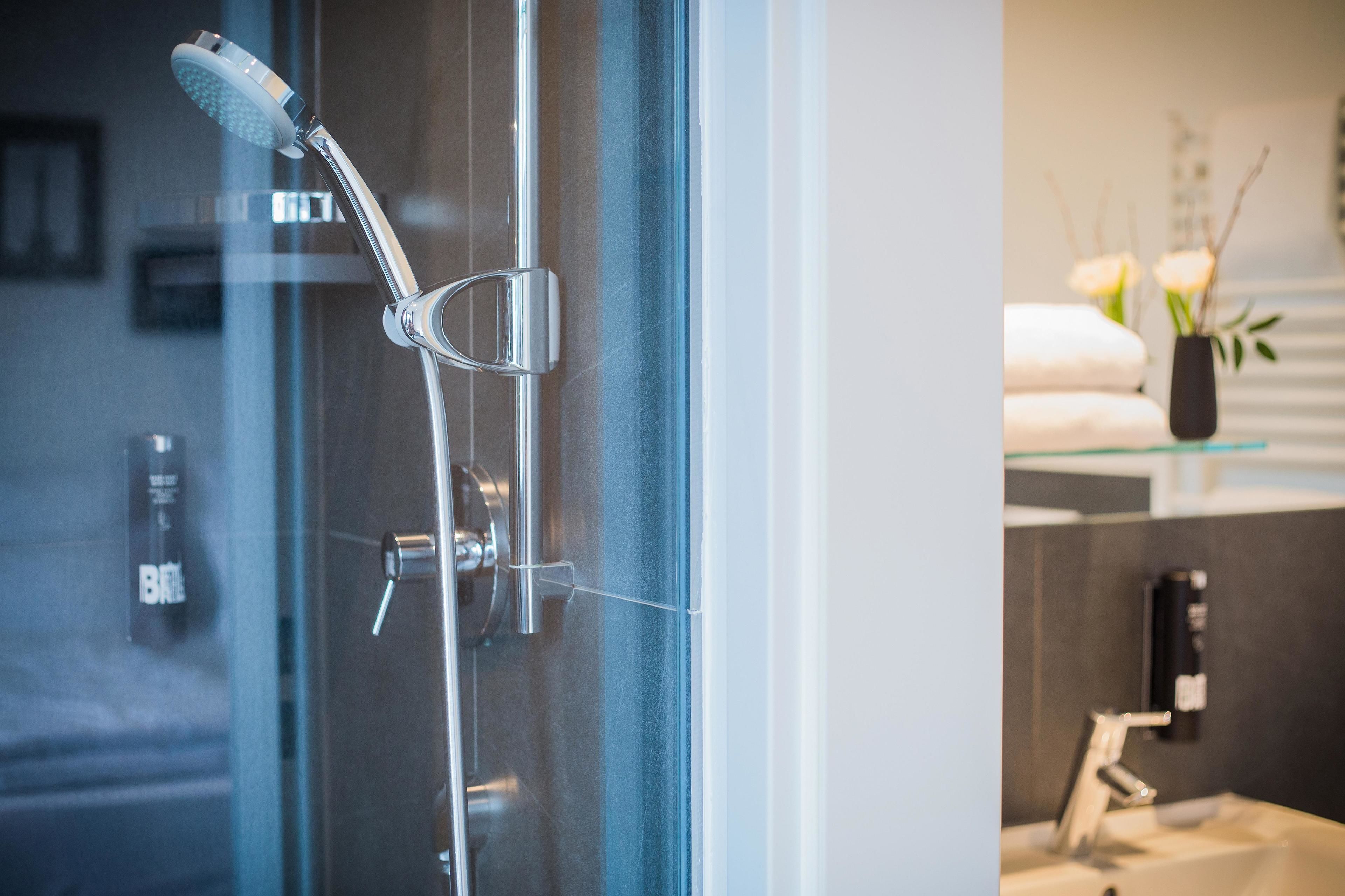 Ein modernes Badezimmer mit Duschkabine aus Glas, sichtbarer Bedienungsplatte und Waschtischbereich mit Handtuchhalter.