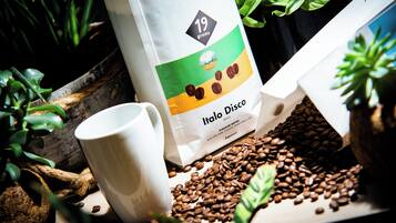 A coffee bag labeled 'Italo Disco' with a 19-gram weight indication, a white mug, and scattered coffee beans.