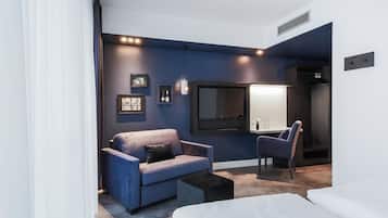 Una habitación de hotel moderna con una pared de acento azul, un televisor de pantalla plana grande, un sofá, una silla y una cama.