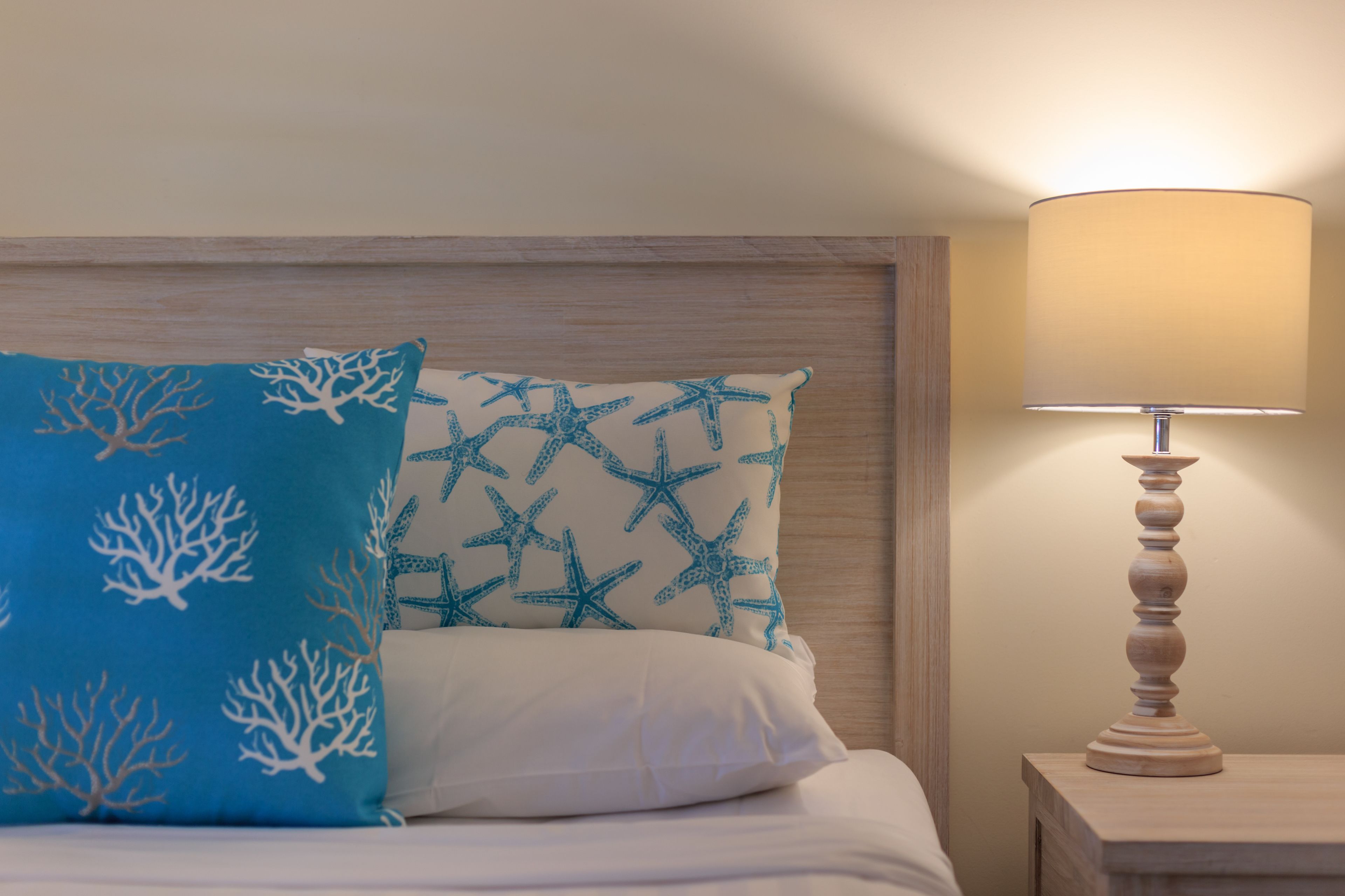 A bed with two pillows, one with a blue and white pattern and the other with a white and blue pattern. There is a wooden nightstand with a lamp on it.