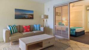 A modern living room with a sofa, a coffee table, and a painting of a beach scene. - Macrossan House (Port Douglas)