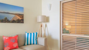 A living room with a beige sofa, a lamp, and a painting of a beach scene. - Macrossan House (Port Douglas)