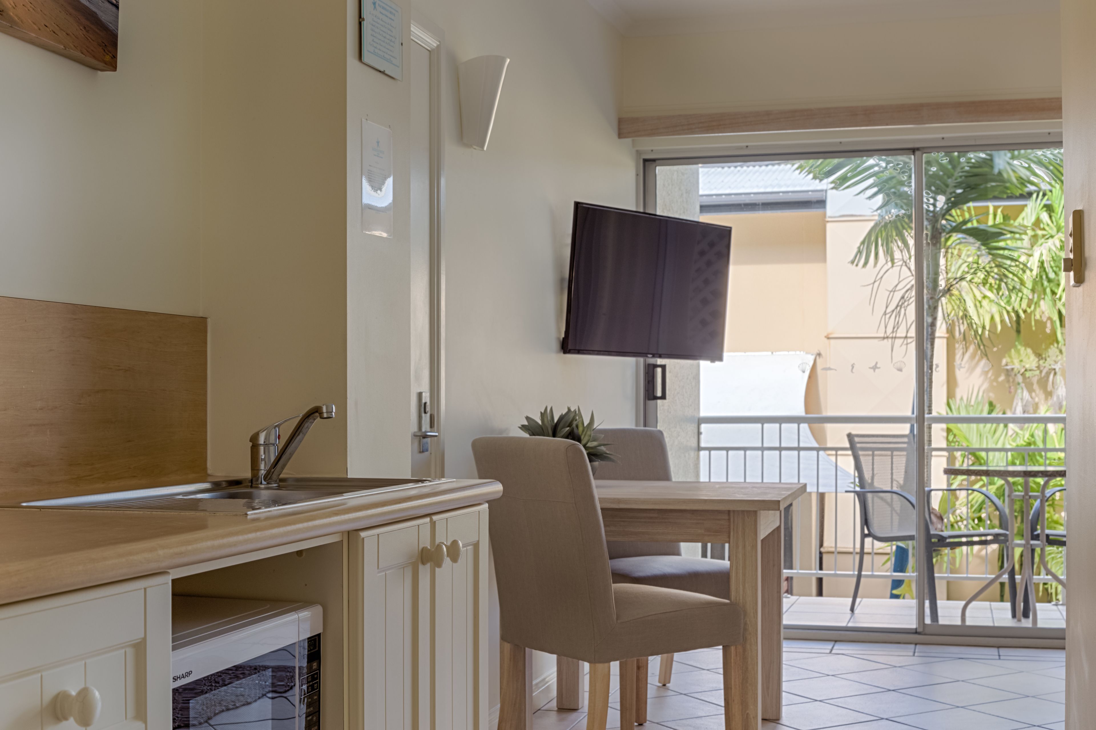 Een moderne keuken met een inbouwvaatwasser, een eethoek met een tafel en stoelen, en een balkon met uitzicht op palmbomen.