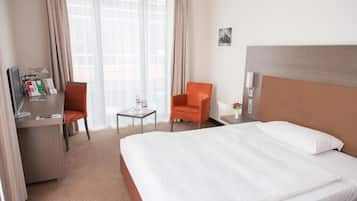 A hotel room with a large bed, a desk with a chair, a small table, and a window with curtains.