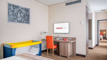 Habitación de hotel con cama, escritorio, silla, televisor y zona de juegos para niños.