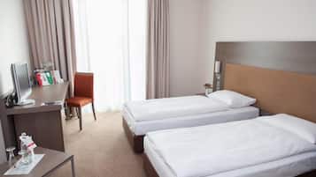 A hotel room with two beds, a desk with a computer, a chair, and a window with curtains.