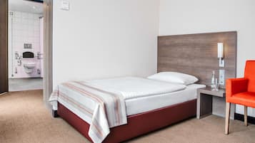A hotel room with a bed, a nightstand, a red chair, and a bathroom visible through an open door.