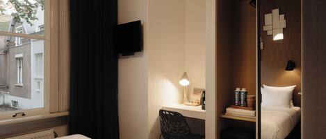 Habitación de hotel con cama, escritorio, silla, televisión y ventana con cortinas.