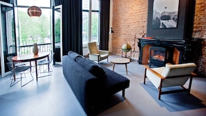 A modern living room with a black sofa, two armchairs, a round coffee table, and a fireplace. There is a large window with curtains, a globe on a stand, and a framed picture on the wall.