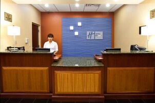 Mostrador de recepción de hotel con una recepcionista, una pared azul con diseño de olas y un letrero de Holiday Inn Express.