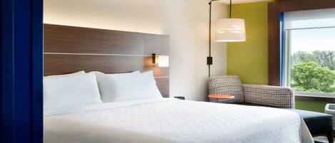 Et hotelværelse med en stor seng, et natbord, en lampe, en stol og et vindue med udsigt.