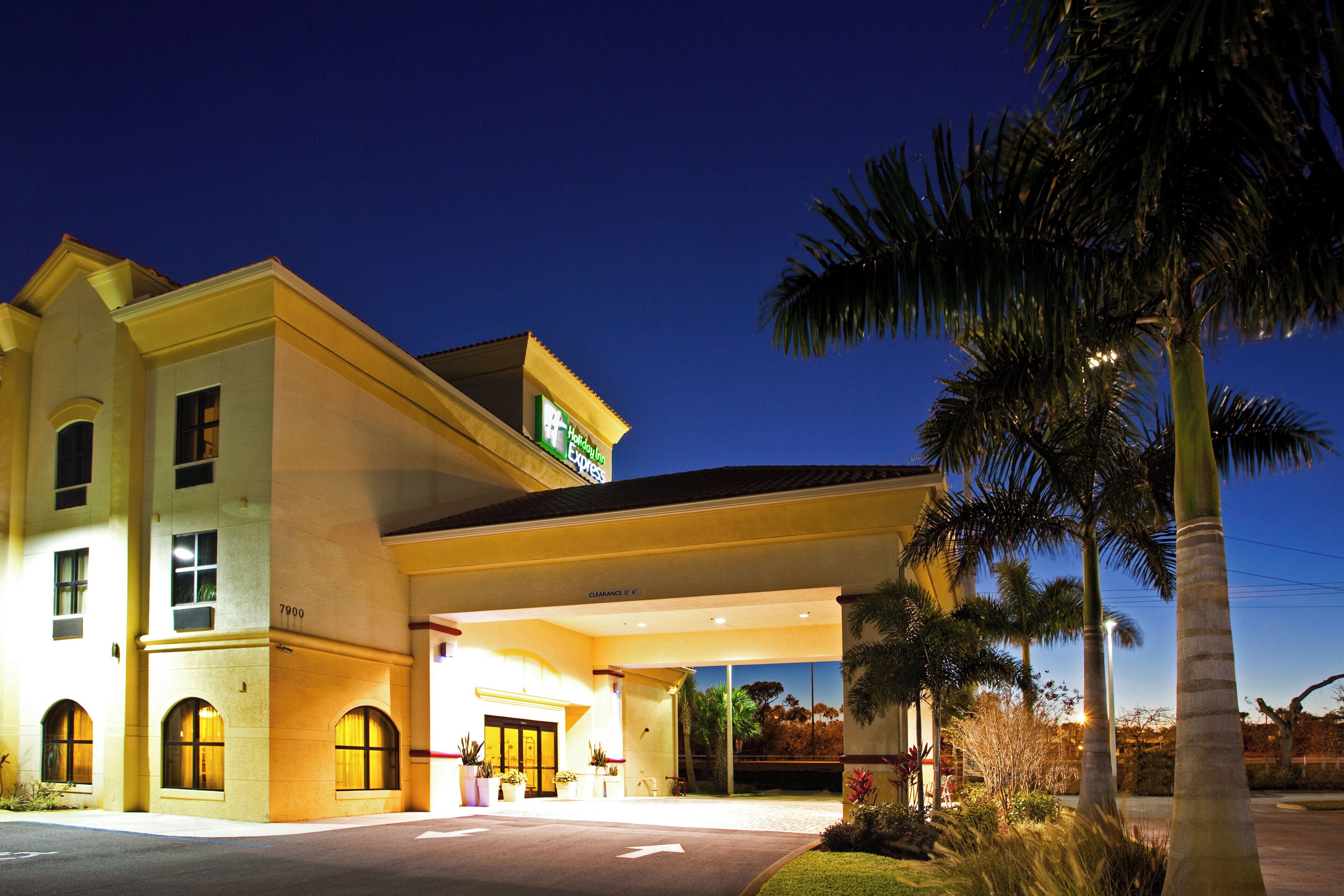 A hotel with a covered entrance, palm trees, and a clear sky.