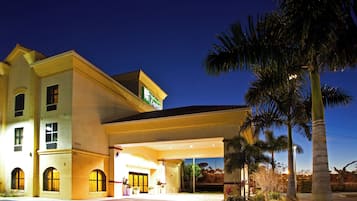 A hotel with a covered entrance, palm trees, and a clear sky.