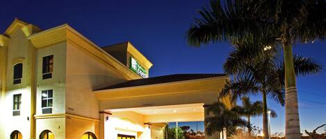 A hotel with a covered entrance, palm trees, and a clear sky.