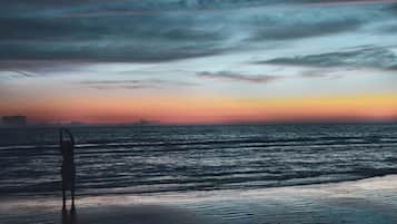 A beach with a person standing in the foreground, waves in the background, and a sunset sky.