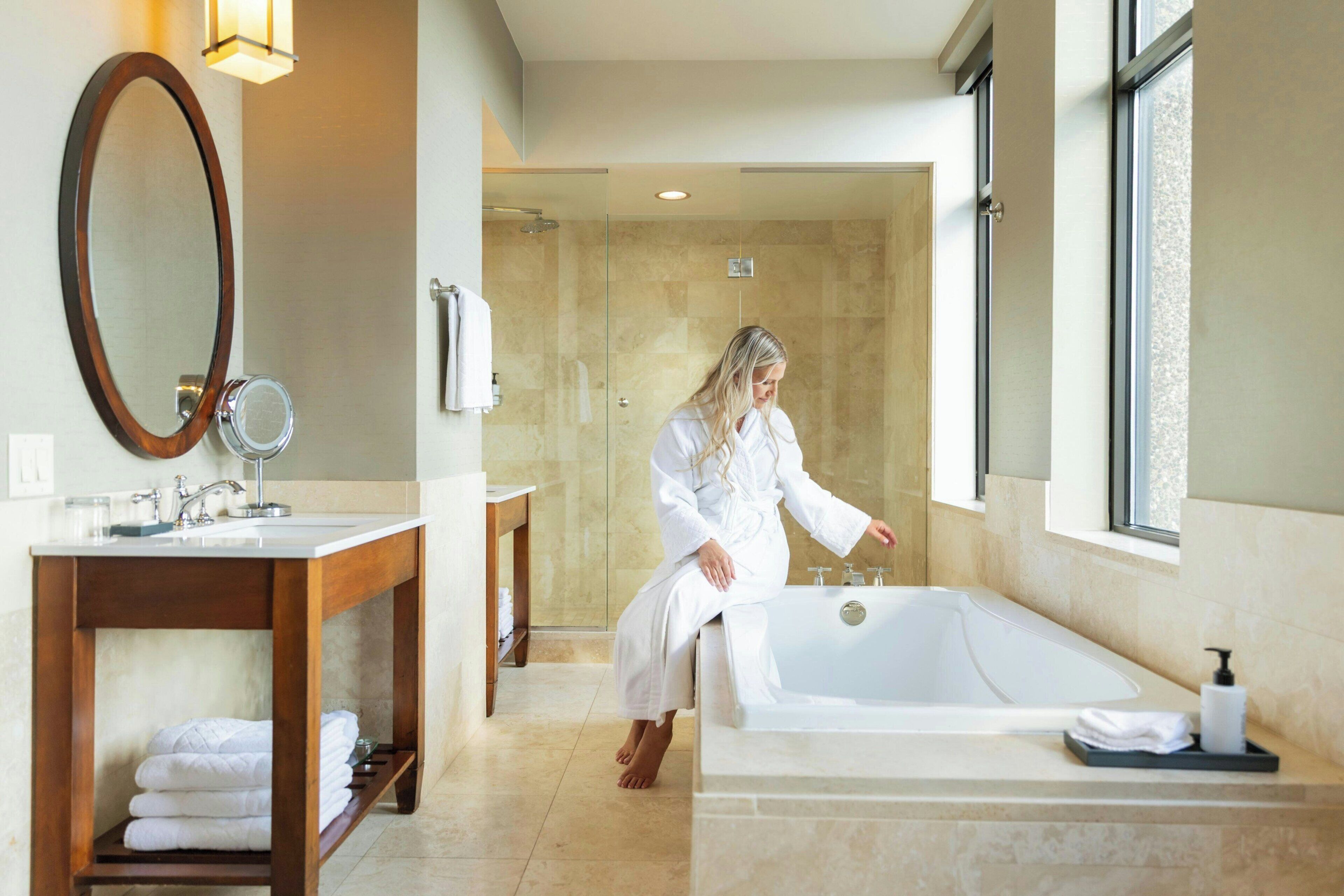 A modern bathroom with a large bathtub, a wooden vanity, a mirror, and a glass shower enclosure.