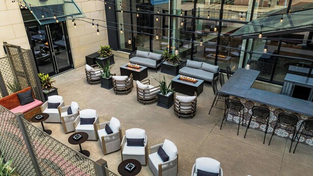An outdoor seating area with various chairs and tables, some with built-in fire pits, surrounded by potted plants and a glass railing. - Hotel Ivy, a Luxury Collection Hotel, Minneapolis (Minneapolis)
