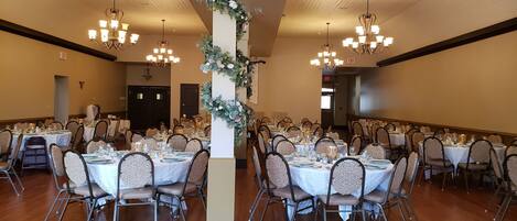 A banquet hall with round tables set for dining, chandeliers, and a decorative floral column.