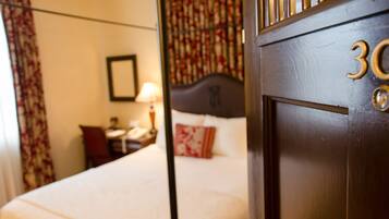 Habitación de hotel con cama, mesita de noche, lámpara y ventana con cortinas.