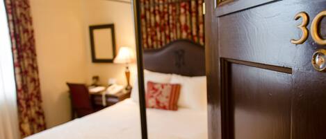 A hotel room with a bed, a nightstand, a lamp, and a window with curtains.
