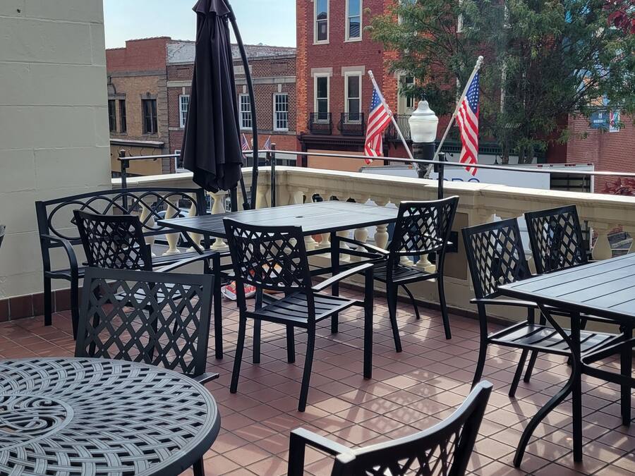 A terrace with outdoor seating, including round and square tables and chairs, and two American flags.