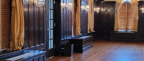 A spacious room with wooden flooring, dark wooden cabinets, and large windows with golden curtains.