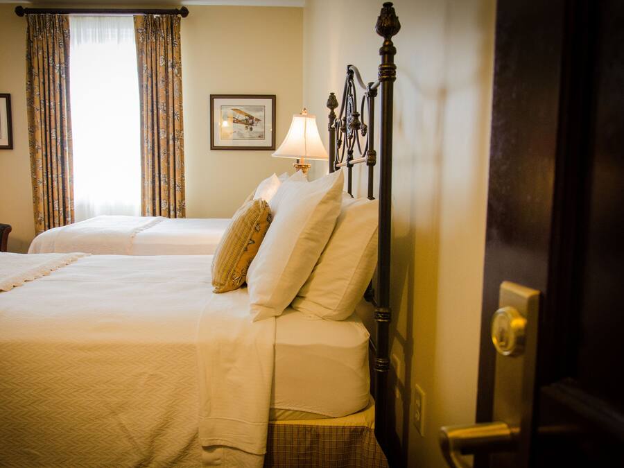 A hotel room with two beds, a nightstand with a lamp, and curtains.