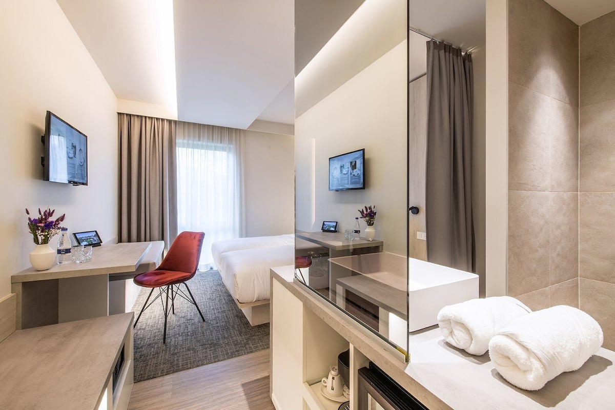 Quarto de hotel com escrivaninha, cadeira, cama, televisão e chuveiro.