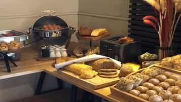 A buffet with various breads, pastries, and a hot grill.