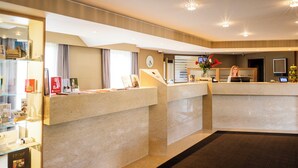 A hotel reception area with a marble counter, a clock, and a receptionist. - Begijnhof Hotel (Leuven)